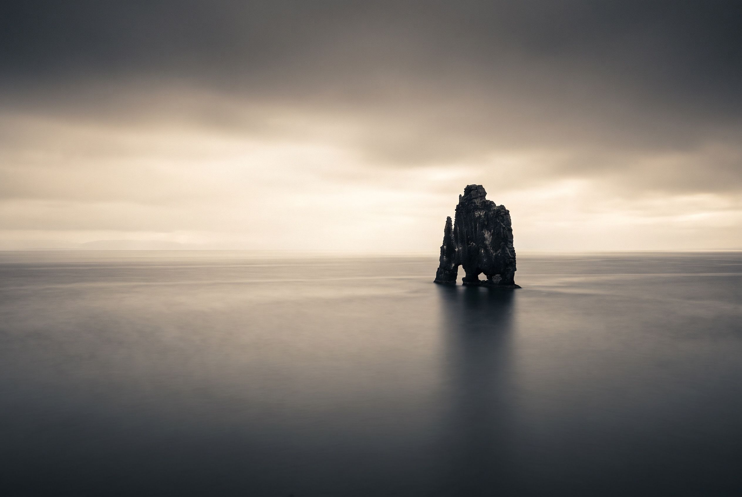 A dark sea stack against still water